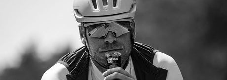 Sort-hvidt actionbillede af en cykelrytter, der indtager en energigel under træning, som illustrerer test af gels, timing og energiindtag i udholdenhedssport.